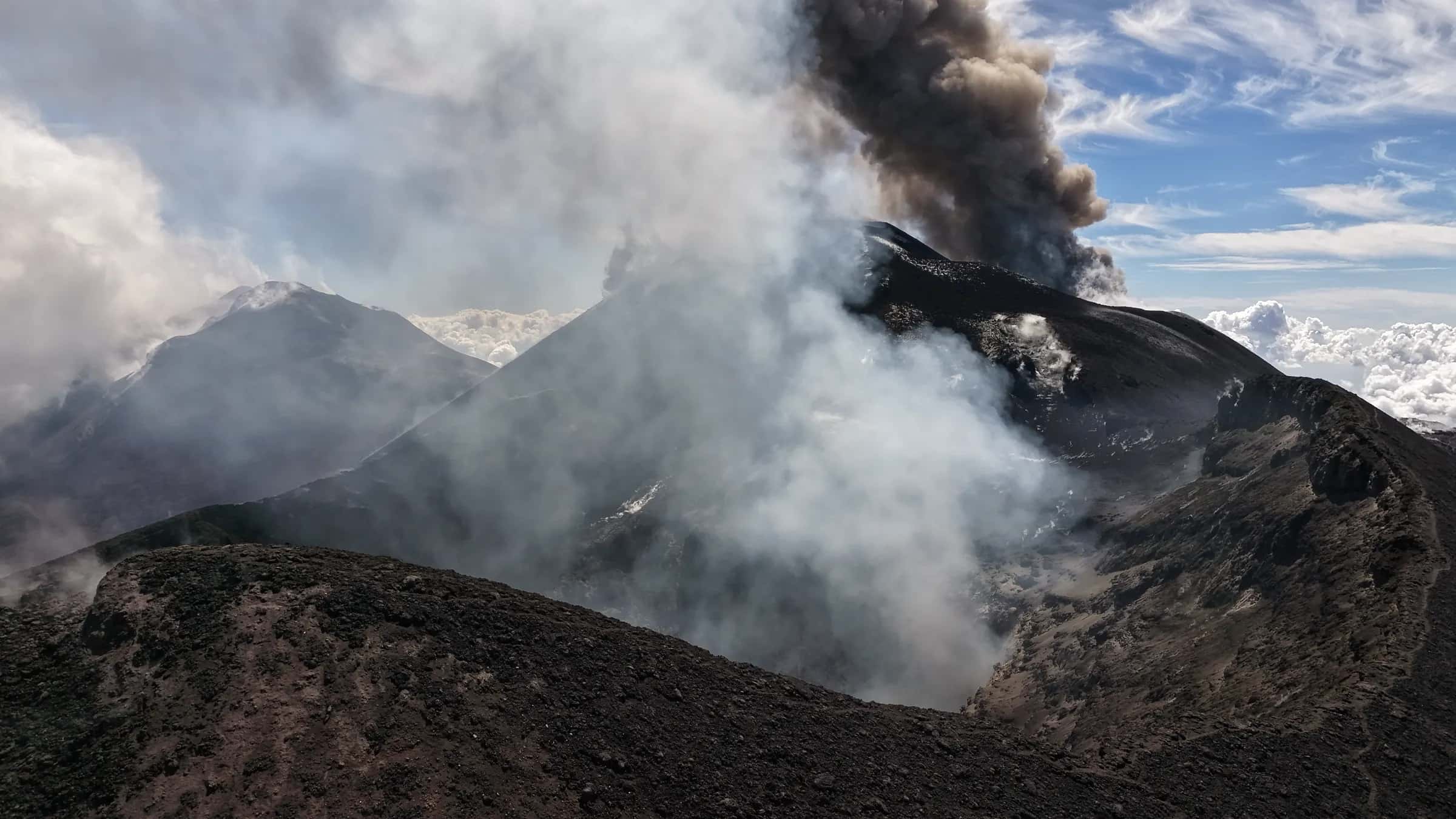 I crateri sommitali visti dal drone, tra vapori bianchi e una colonna di cenere