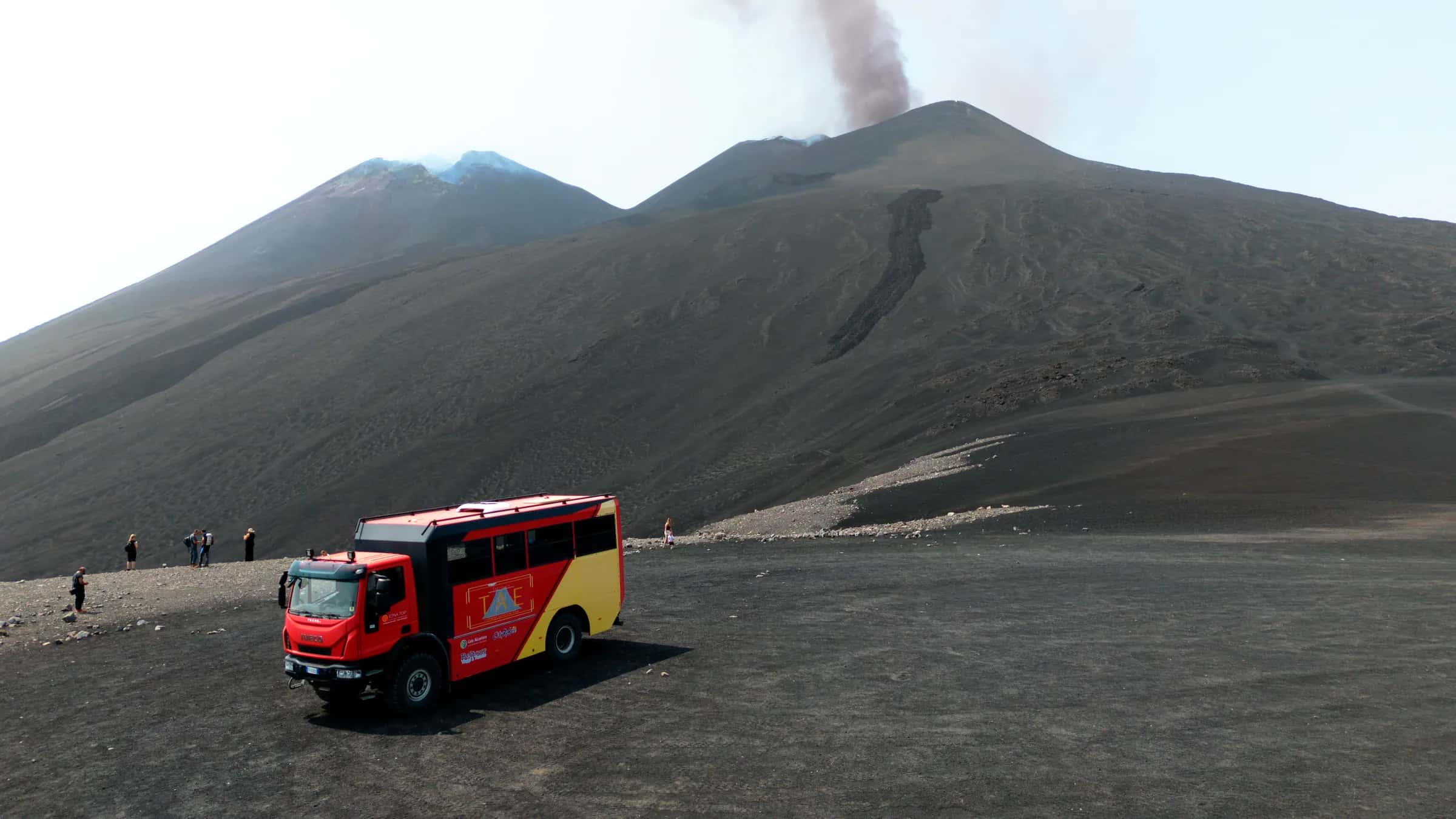 Il bus 4x4 rosso sulla cenere in quota, con i crateri sommitali e il pennacchio alle spalle
