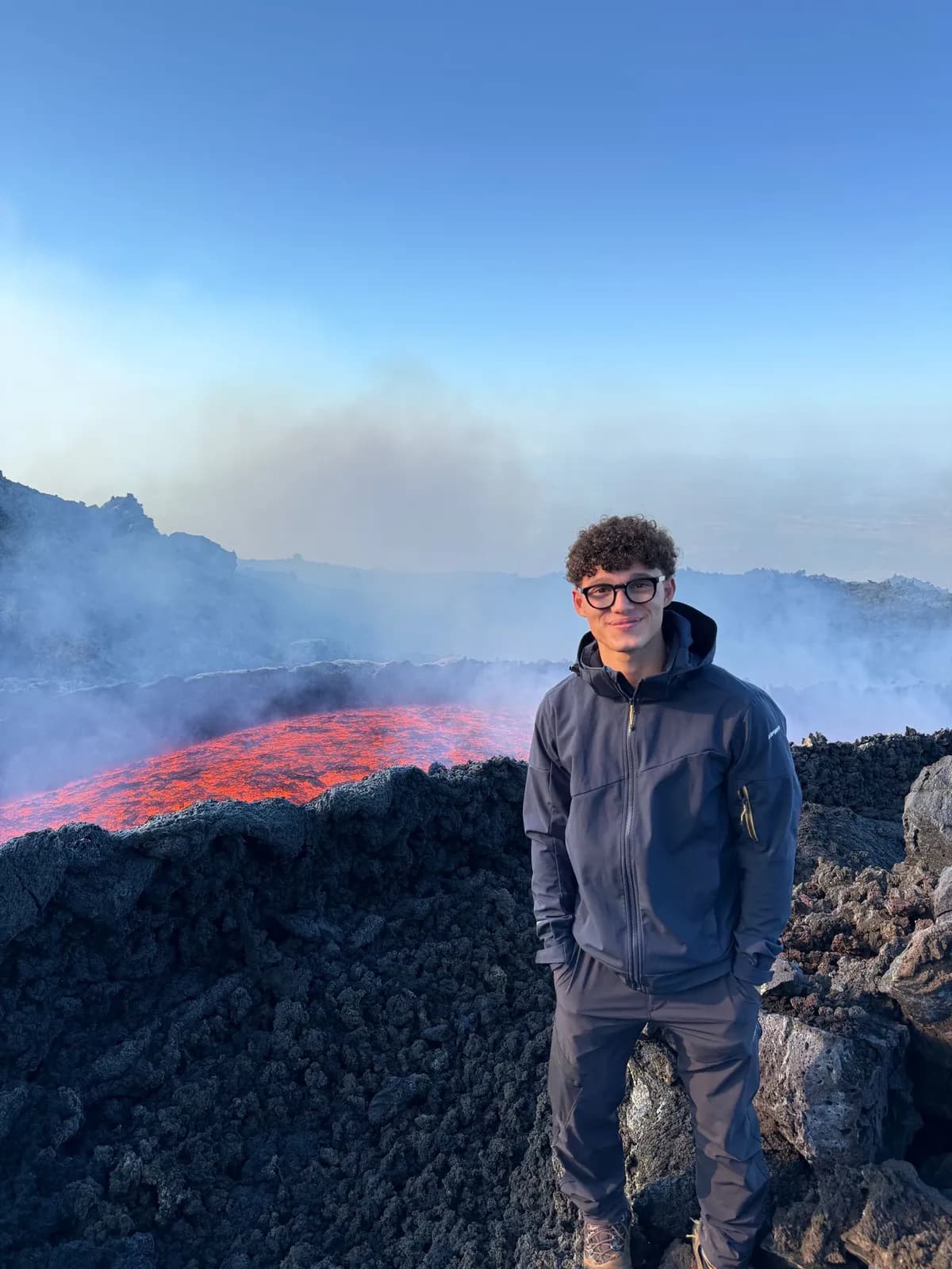Flavio sorride davanti a una colata di lava incandescente, con il fumo che sale alle sue spalle