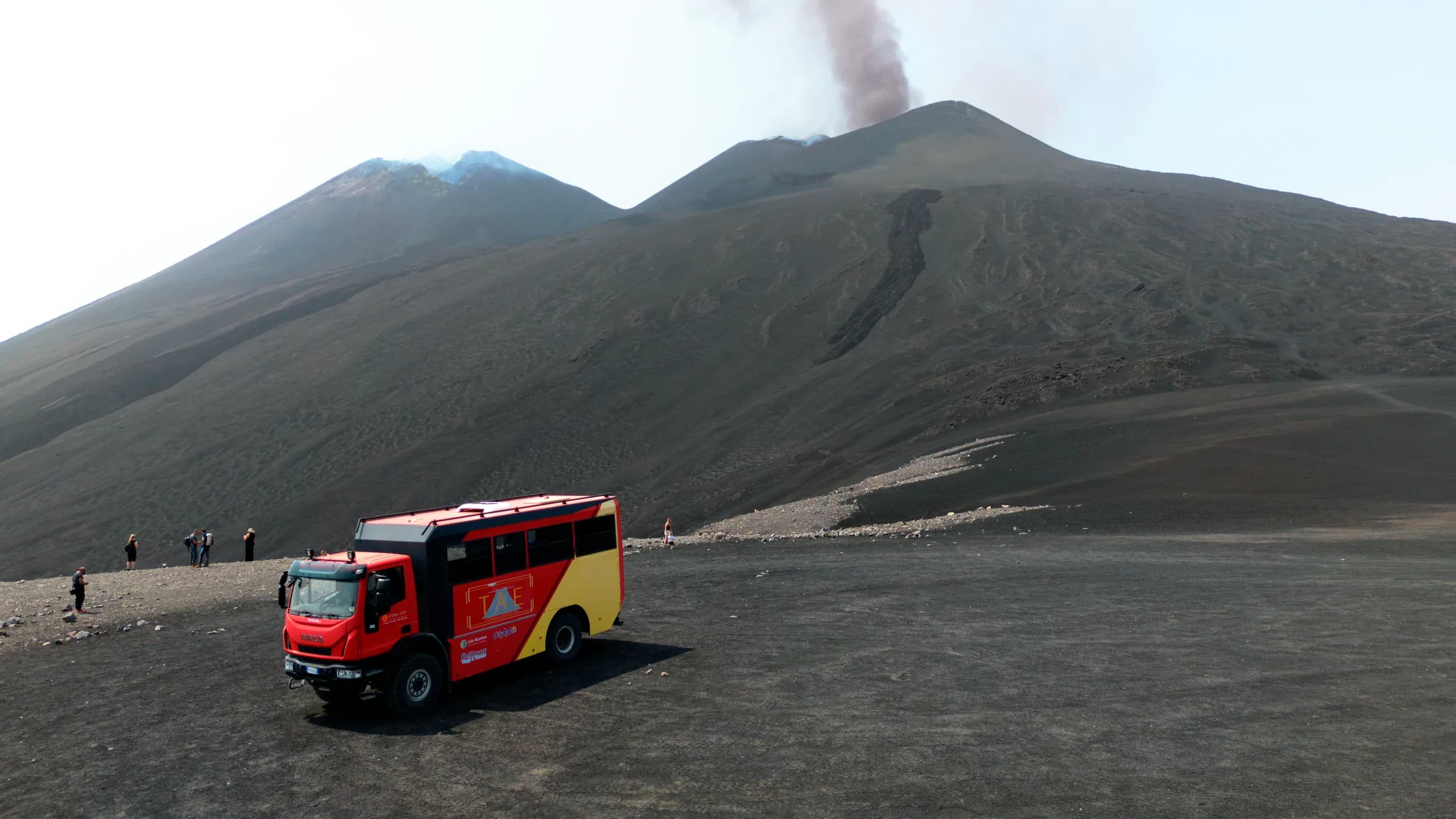 Il bus 4x4 rosso sulla cenere in quota, con i crateri sommitali e il pennacchio alle spalle